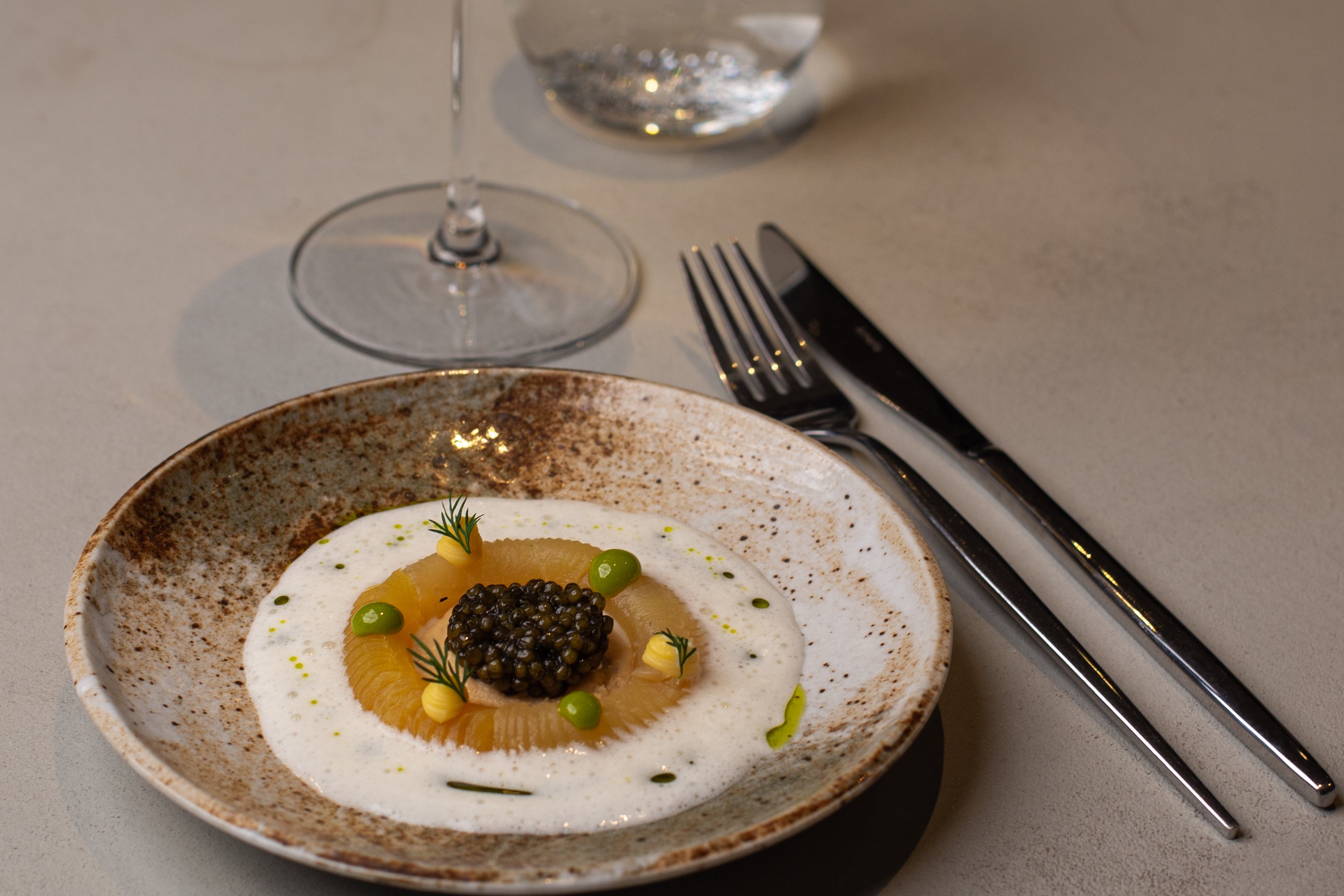 A caviar dish with wine and water glasses from the Skóg menu